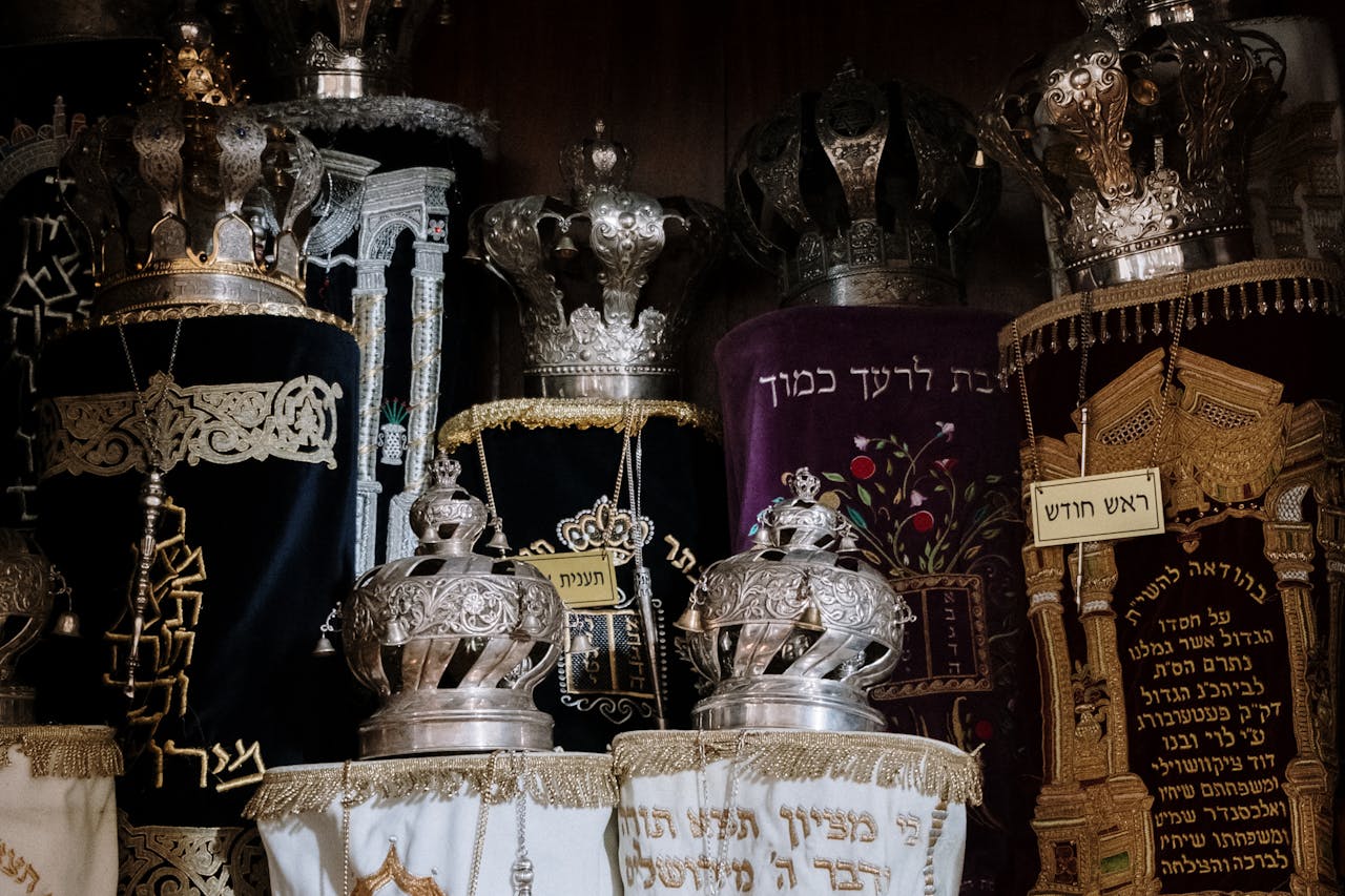 Intricately adorned Torah scrolls with silver crowns in a synagogue setting.